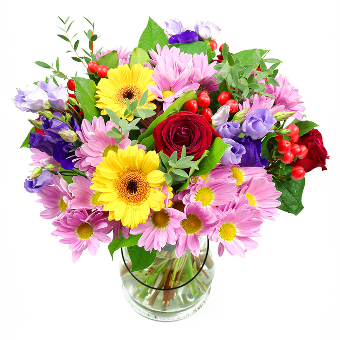 The photograph shows a vibrant mixed bouquet standing tall in a clear glass vase, placed against a smooth white background so all the flower colours and shapes appear crisp and defined. Dominating the centre are velvety deep red roses, their rich petals layered in tight spirals that convey romance and a grounded sense of tradition. Beside them, striking yellow gerbera daisies with dark, warm brown-orange centres act like sunbursts, creating a joyful focal point that instantly lifts the mood. Encircling these bold blooms, an abundance of pastel pink daisies and chrysanthemums stretches outward, their many slender petals and tiny yellow centres giving the bouquet a soft, cloud-like fullness. Threaded through and rising just a little higher, purple and lavender lisianthus flowers add a graceful, bell-shaped elegance, introducing cooler tones that balance the intensity of the reds and yellows. Dotted among the blossoms, small clusters of shiny, rounded red hypericum berries lend a modern, textural touch, almost like beads or tiny cherries tucked in for fun. Framing everything is a varied selection of fresh greenery, from broad, dark leaves to fine, delicate sprigs in lighter green, which enhances the feeling of natural abundance and freshness, as if the bouquet might have been crafted from blooms gathered around Colliers Wood's leafy pathways. Clear water and neatly trimmed stems are visible through the vase, reflecting the careful construction and thoughtful design of an experienced florist. The overall atmosphere is warm, uplifting, and celebratory, ideal for birthdays, thank-yous, or get-well wishes in SW19. It's the kind of bouquet you could imagine arriving at a home off Christchurch Road, immediately becoming a colourful, welcoming centrepiece on the dining table.